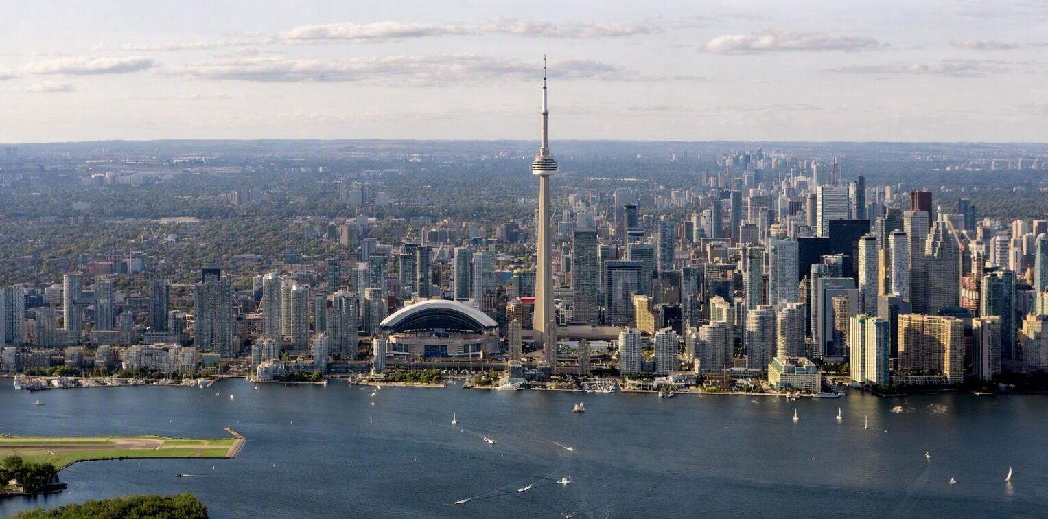 Aerial view of downtown Toronto featuring the CN Tower, Rogers Centre, and Lake Ontario with boats and islands in the foreground.